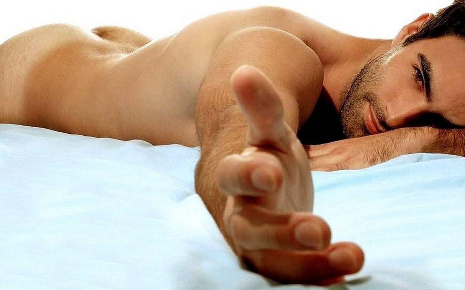 небритый мужчина лежа на животе в голом виде протягивает руку к камере, фото красивого мужчины